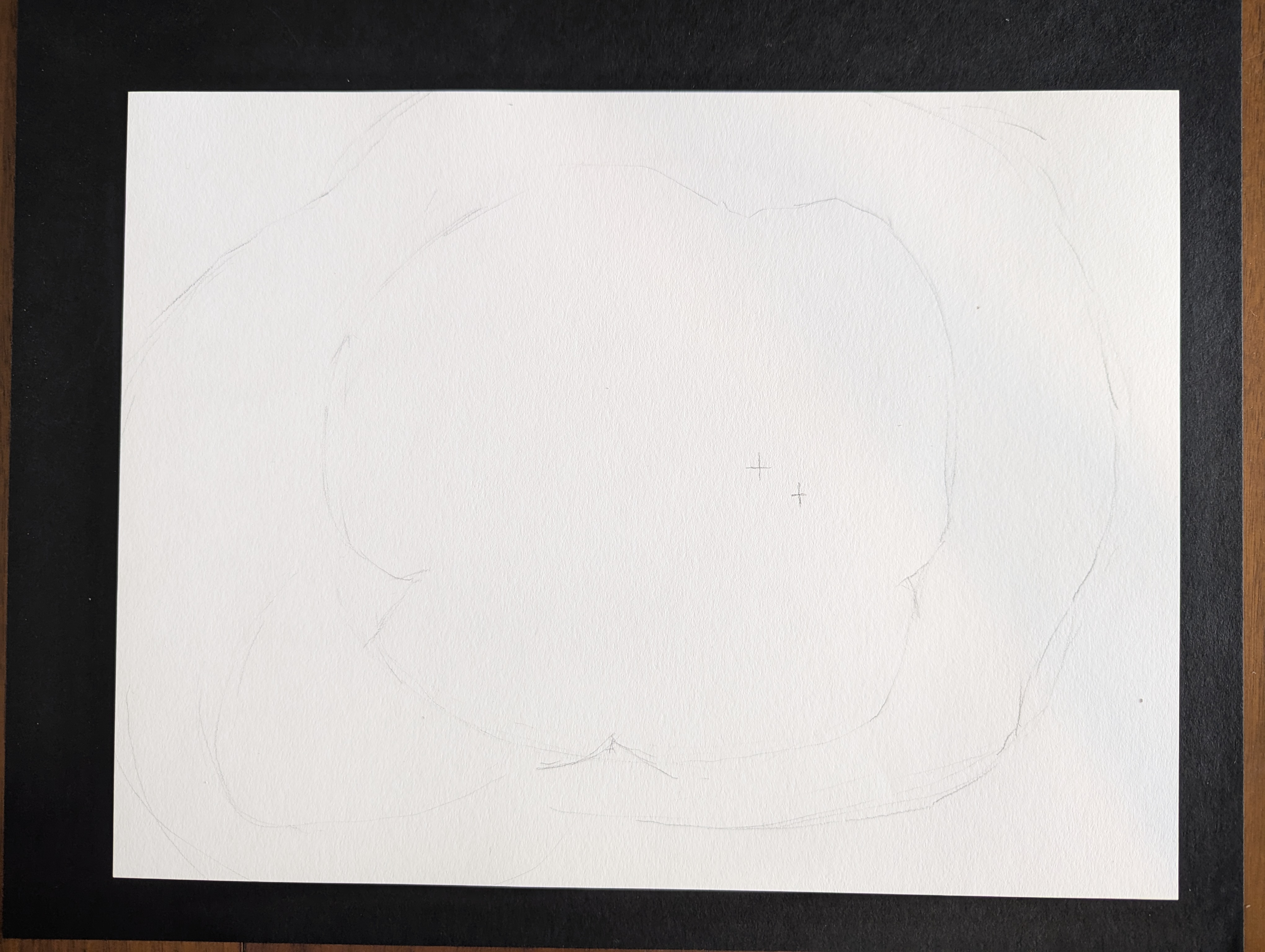 Photo of a white sheet of watercolor paper with some lightly sketched shapes against a black tabletop.