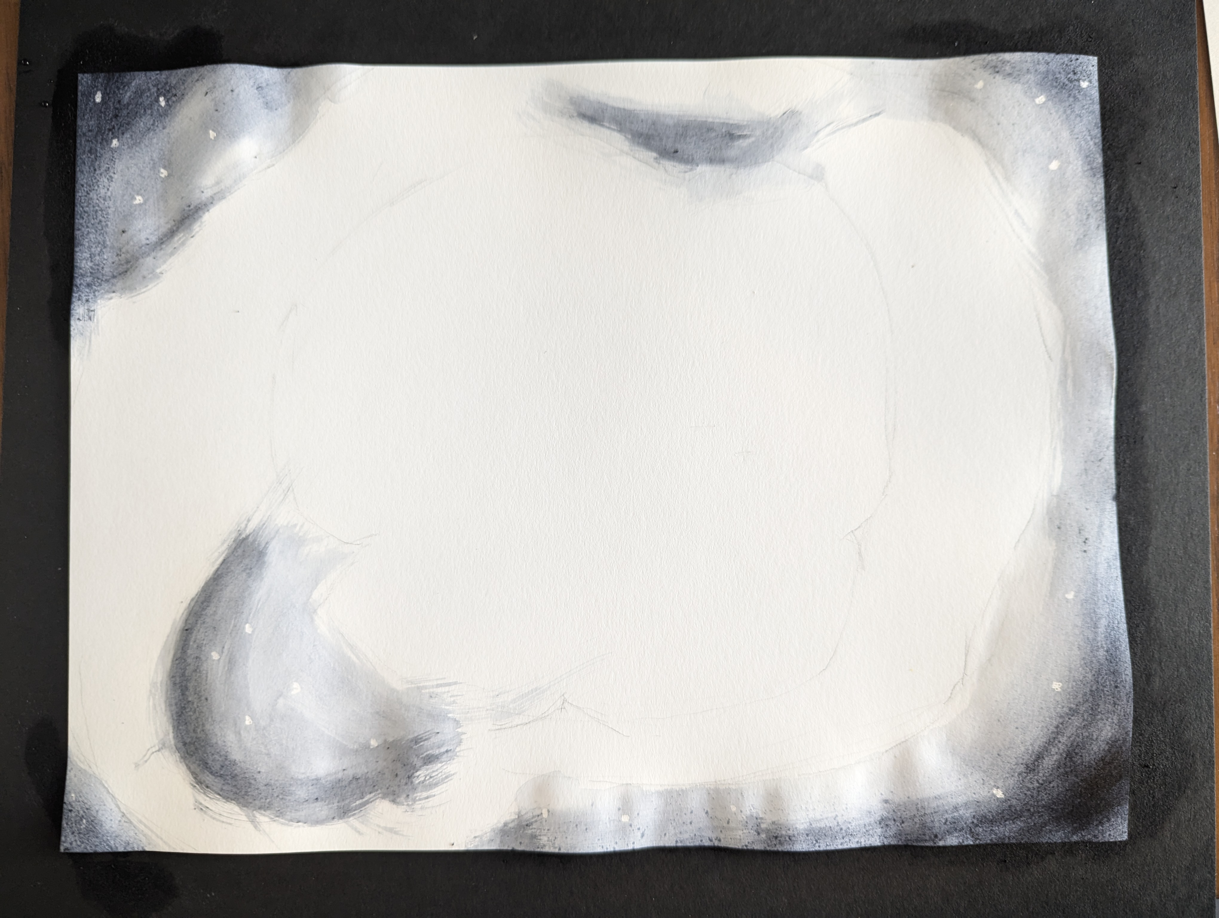 Photo of a white sheet of watercolor paper with some lightly sketched shapes against a black tabletop. The edges of the paper have been painted dark gray, and there are stars. 