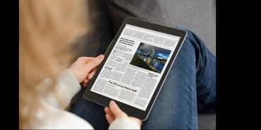 Hands holding a tablet or reader displaying articles