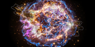 Supernova remnant Cassiopeia A imaged by the Chandra X-ray Observatory. Cassiopeia A is a roughly circular cloud of multicolored gas and debris against a black background. The outer edges of the circle are mostly wispy filaments of bright blue gas. Within the blue outer shell, there are clumps of green, purple, yellow, and orange gas. Striated filaments of bright blue are in the center of the nebula, which surround a tiny white dot. A white dashed line outlines the shape of a portion of the remnant.