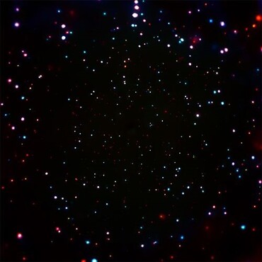 Chandra Deep Field. Against the black background of space are many colorful points of light: white, red, orange, yellow, blue, and purple. The points of light tend to be smaller closer toward the image’s center, while those toward the edges are slightly bigger in size.