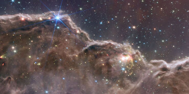 Bright stars in a range of sizes are scattered across a dense gray-brown undulating cloudscape at bottom and deep purple space at top.