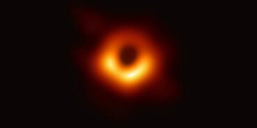 Event Horizon Telescope image of the black hole at the center of the Milky Way galaxy, Sagittarius A. It resembles a slightly oblong donut-shaped ring of glowing, warm dust. Within the ring, there are especially bright areas at the top, left, and right.