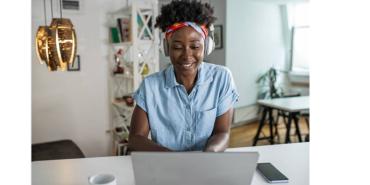 Smiling woman wearing headphones, writes in a notebook and works on a laptop