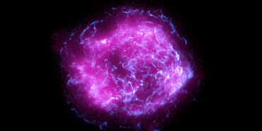Supernova remnant Cassiopeia A as imaged by the Imaging X-ray Polarimetry Explorer (IXPE) satellite and Chandra X-ray Observatory. Cassiopeia A is a circular-shaped cloud of bright purple and pink mottled material against a black background. Some of the material, most notably toward the remnant’s exterior, has a bright purple glow.