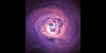 The Perseus Cluster as imaged by the Chandra X-ray Observatory. A small, bright white blob is in the center surrounded by wispy material resembling the thread-like texture of cotton candy. The surrounding material is white near the central white blob and gradually dims to shades of pink, purple, and black moving further away. A thin, blue-white band of material is on the right side of the bright central blob. A few small pink-white specks of light are scattered across the top half of the image.