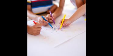 Children's hands drawing on paper with colorful markers