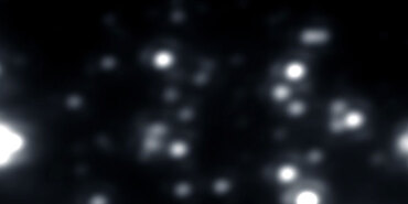 Image of a dark swath of space. Blurry, faint white blobs of differing definition, which are stars, are scattered across.