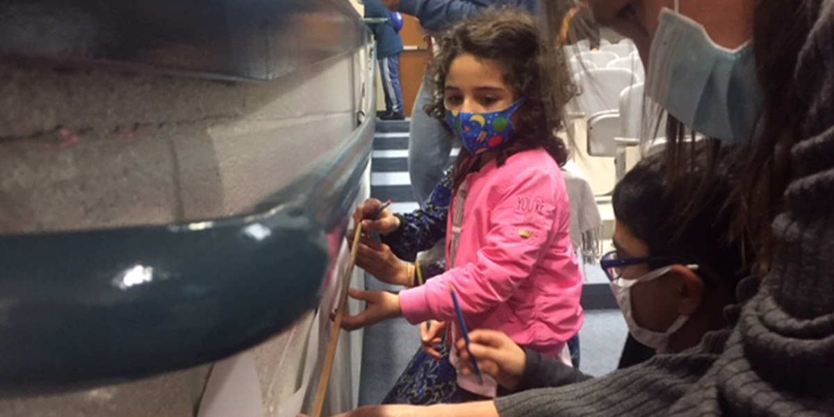Two children standing next to a wall.