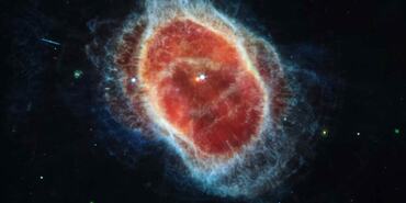 The image shows two stars at the center very close to one another. The one at left is red, the one at right is light blue. The blue star has tiny diffraction spikes around it. A large translucent red oval surrounds the central stars. From the red oval, shells extend in a mix of colors.