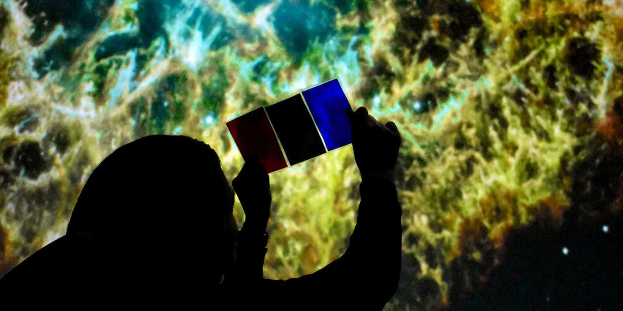 person holding up paper with astronomical image behind