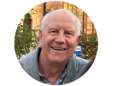 A smiling medium white-skinned man with short white hair,  wearing a pale blue Hawaiian shirt. 