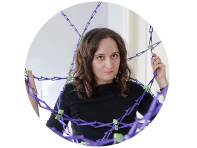 A woman stands inside a purple Hoberman sphere, an expanding sphere toy.