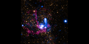 The center of the Milky Way galaxy. Golden orange specks of light and tendrils of neon purple and blue clouds are set against a black background. The oranges and purples were captured in infrared light by the Hubble Space Telescope. The blues represent data from the Chandra X-ray Observatory. At the heart of the main image are several bright white dots, including one that contains the supermassive black hole at the center of our galaxy, known as Sagittarius A*.